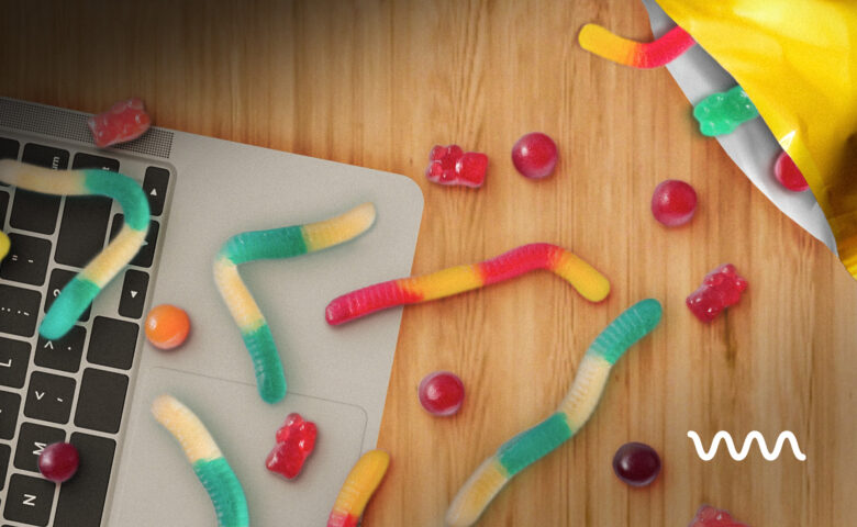 Colorful gummy worms and candies scattered on a laptop keyboard and wooden desk surface.
